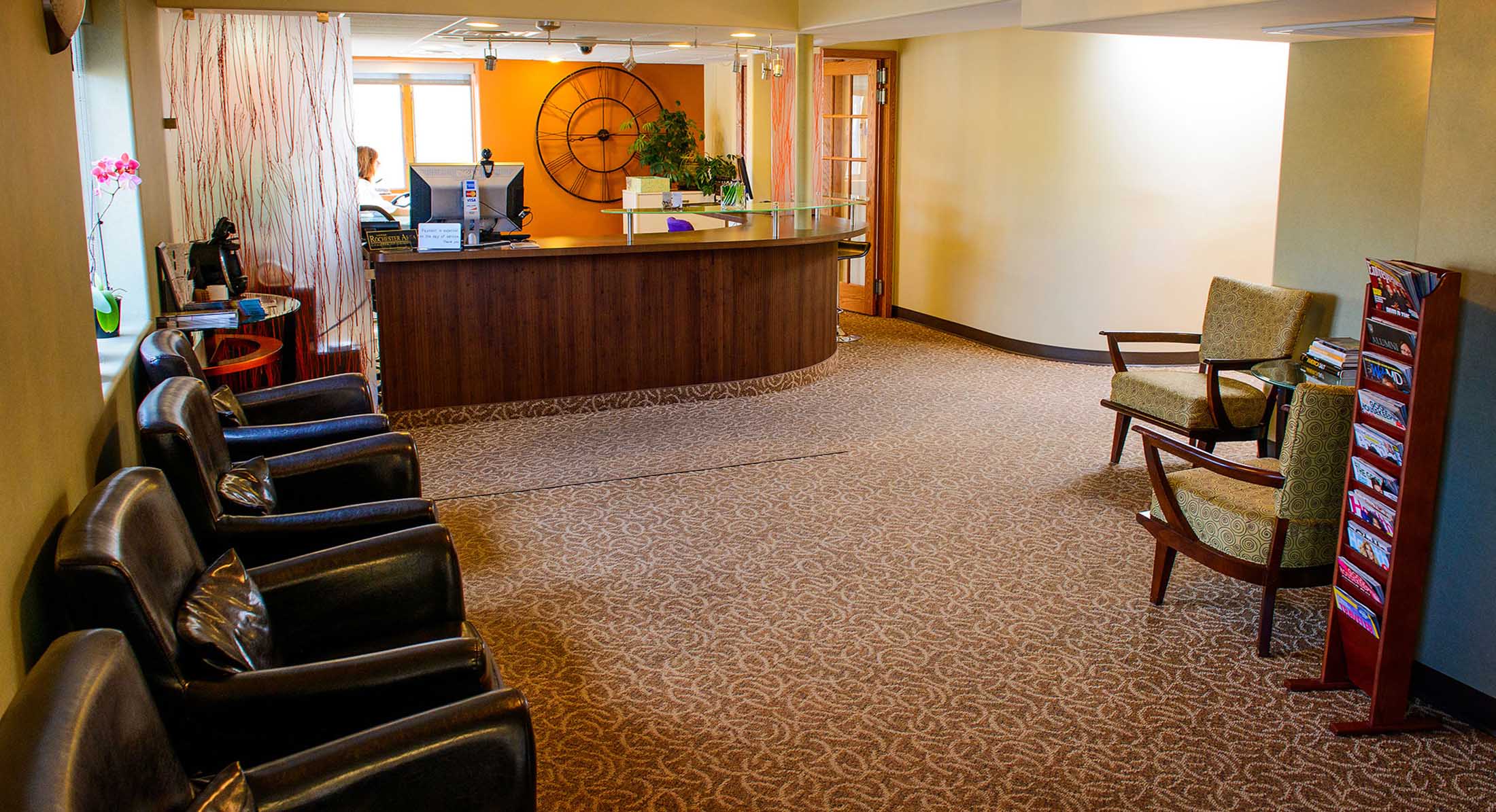 The image shows an interior view of a lobby with a reception desk area, featuring a seating arrangement with chairs and a carpeted floor.