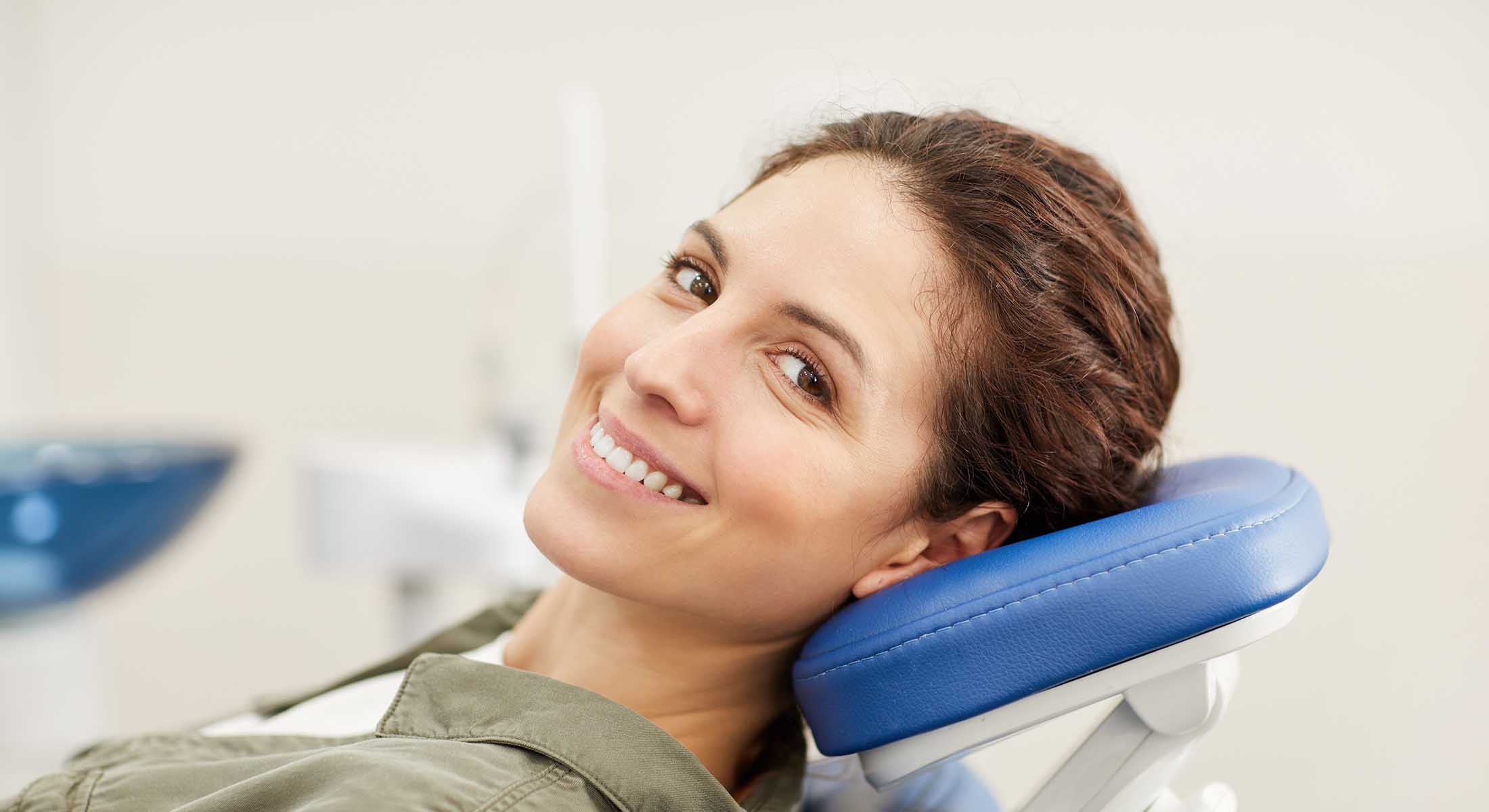 A woman with a smile sits in a dental chair during a dental appointment.