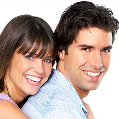 A man and woman posing closely together with smiles on their faces against a white background.