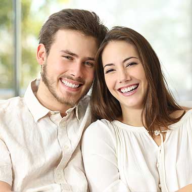A young couple smiling at each other, with the man on the left and the woman on the right, both seated and posing for a photo.