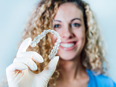 A woman wearing a white glove holds up a large, clear plastic dental retainer.