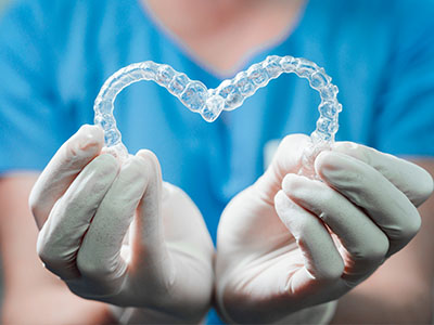 A dental professional s hands cradling a heart-shaped transparent object resembling a mouthguard, symbolizing dental care.