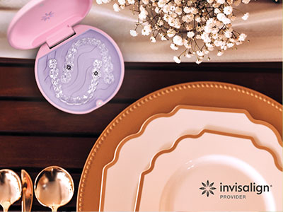 The image displays a collection of tableware items including plates, bowls, and a spoon rest, arranged on a wooden surface with a pink lid from a cosmetic product in the background.