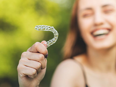 A young woman with a radiant smile holds up a clear dental retainer.