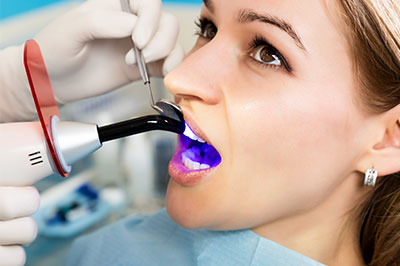 A woman receiving dental treatment with a dentist using a specialized device to clean her teeth.