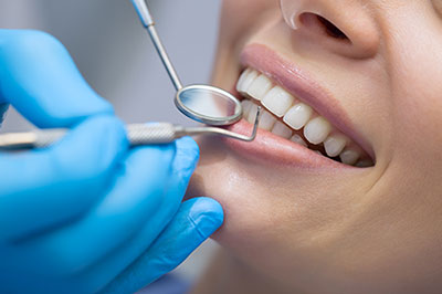 The image shows a person receiving dental treatment  they are seated with their mouth open and wearing a blue surgical gown, while a dental professional works on them using dental instruments.