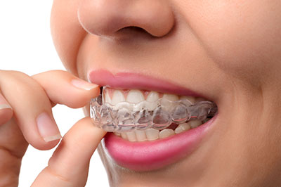 A woman with braces is holding her finger near her mouth.