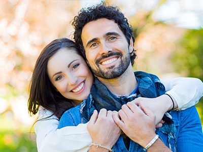 A young couple embracing each other outdoors with a joyful expression.