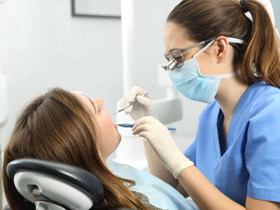 The image shows a dental hygienist performing a cleaning procedure on a patient s teeth while wearing personal protective equipment, including gloves and a mask.