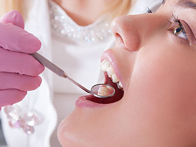 A dental professional is performing a dental procedure on a woman s mouth using dental instruments.