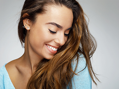 A young woman with long hair smiles at the camera against a neutral background.