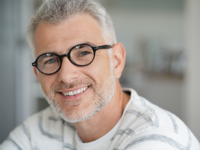 Man with gray hair smiling at camera, wearing glasses and a patterned shirt.