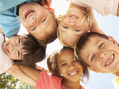 A group of children with different facial expressions are huddled together, smiling at the camera.