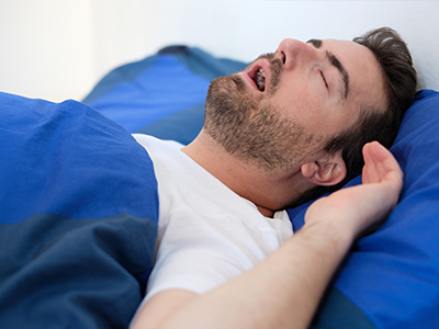 A man is lying down on a bed with his eyes closed, appearing to be asleep or resting.