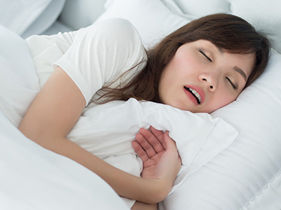 A woman lying in bed with her eyes closed, wearing a white shirt, and holding a pillow over her mouth.