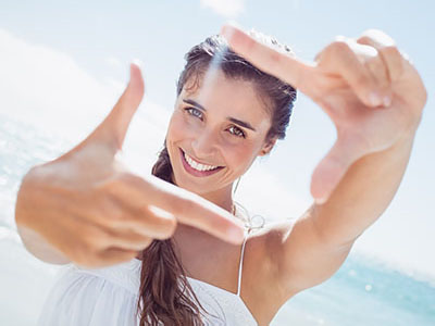 A woman with long hair is smiling at the camera while holding up her hand with fingers extended to make an  O  shape, suggesting a playful or celebratory mood.